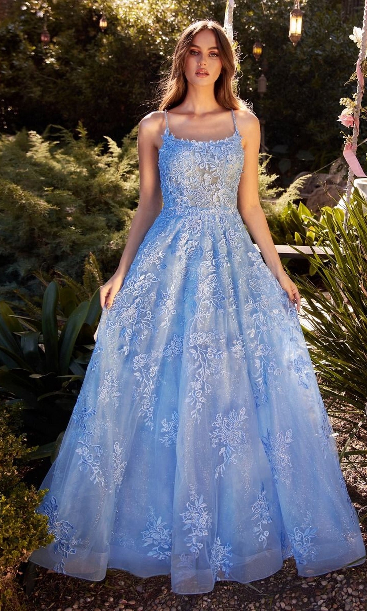 A woman stands outdoors in the Andrea & Leo A1248, an Embroidered Prom Ball Gown featuring a light blue sleeveless design, floral embroidery, and a full skirt.